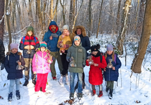 Dzieci, rodzice i opiekunowie pozują do zdjęcia na tle osnieżonych drzew.